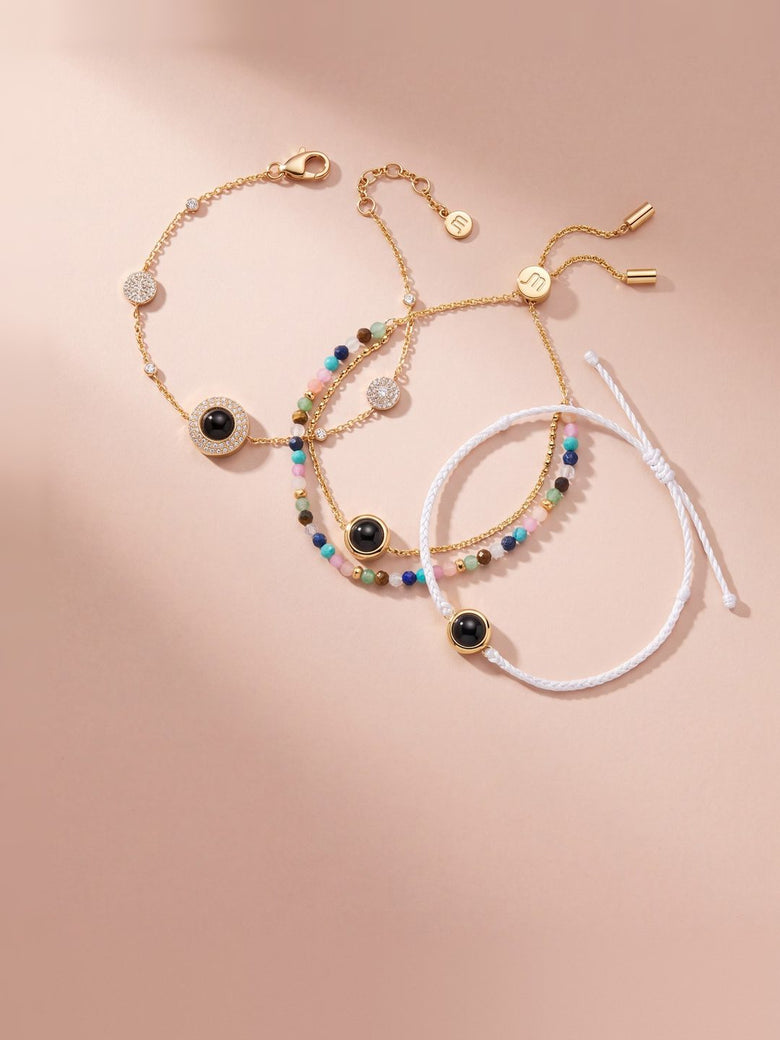 Three gold photo bracelets with black photo gems (pavé chain, colorful beads and white cord) on blush paper
